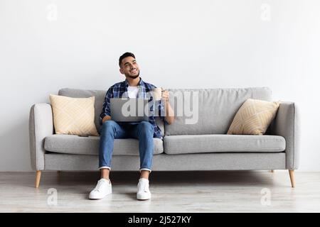 Man using pc sitting on the couch, drinking coffee Stock Photo