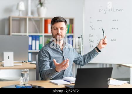 Male english teacher giving remote lesson via laptop, communicating with students on webcam at office interior Stock Photo