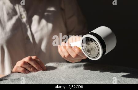 Woman removing lint from fabric with shaver. Handheld electric defuzzer. Clothes care. High quality photo Stock Photo