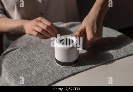 Woman removing lint from fabric with shaver. Handheld electric defuzzer. Cleaning from fuzz, fluff, dust, hair. High quality photo Stock Photo