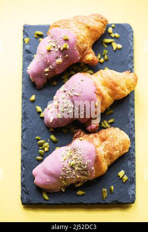 Mini-croissants with ruby chocolate and pistachios on a slate board. Overhed view. Stock Photo
