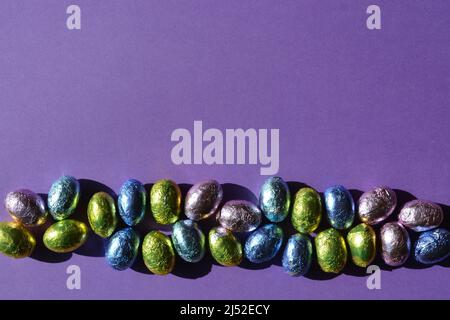 Foil wrapped chocolate Easter eggs isolate on purple background with copy space Stock Photo