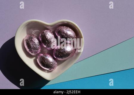 Chocolate Easter eggs in heart shaped dish isolated on colourful pastel background with copy space Stock Photo