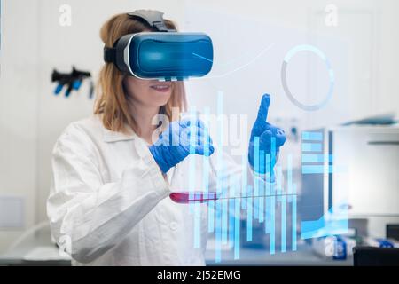Scientist wearing VR goggles, lab coat, holding flask analyse data in Metaverse digital cyberspace with virtual reality. NFT technology of future entertainment.  Stock Photo
