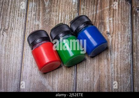 three small plastic paint bottles in the colors red, green and blue on a rustic wooden surface Stock Photo
