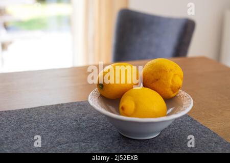 three lemons in a bowl on wooden table indoors Stock Photo