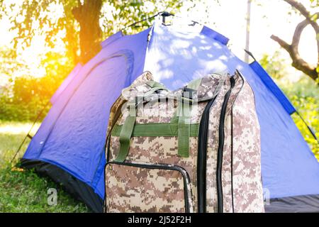 Defocus blue open tourist tent standing on green nature background. Army backpack. Tourism concept. Summer vacation in forest, camping. Wild nature Stock Photo