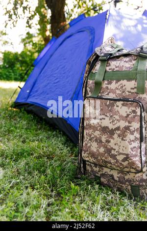 Defocus blue open tourist tent standing on green nature background. Army backpack. Tourism concept. Summer vacation in forest, camping. Lifestyle Stock Photo