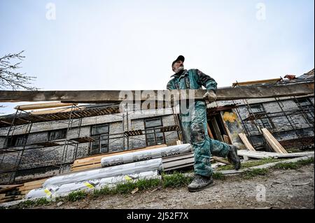 ZAPORIZHZHIA, UKRAINE - APRIL 16, 2022 - A worker carries a wood plank as a 70-year-old building situated on the premises of a military hospital is be Stock Photo
