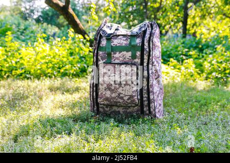 Defocus military backpack. Army bag on green grass background near tree. Military camouflage webbing material on a British army rucksack. Close-up Stock Photo