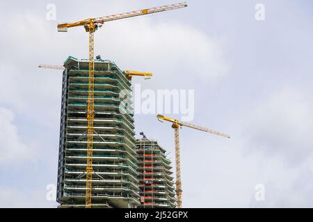 three yellow tower cranes and a fragment of the facade of an unfinished cement building or skyscraper Stock Photo