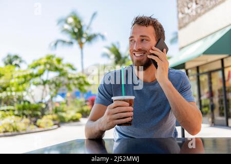Man calling using phone making a call drinking cold coffee drink sitting at cafe terrace holding smartphone talking on mobile smart phone in summer Stock Photo