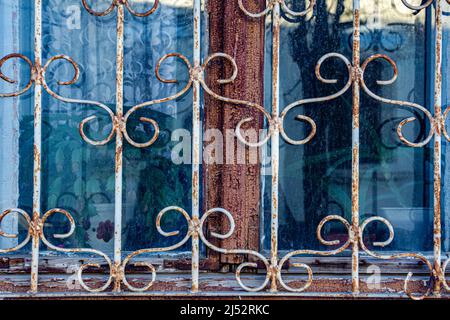 The window of an old house behind a metal patterned lattice. Background image of an old house window with peeling paint and rusted bars. Stock Photo