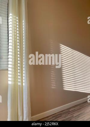 Sunlight streaming in through window blinds making a pattern on the wall Stock Photo