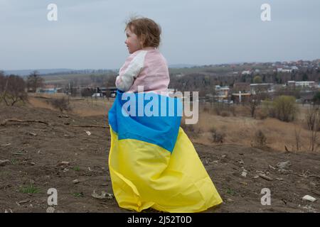 Beautiful baby girl with a flag of Ukraine against the backdrop of a city and a lake in a Ukrainian city. Portrait of a patriotic baby girl with the f Stock Photo