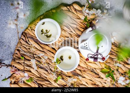 Asian tea pot and cups with green tea and cherry blossom branches Stock Photo