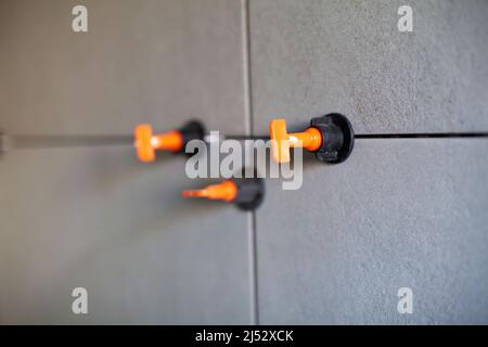 Tile leveling system with plastic clips.Tile leveling system. Tiler installing large format tile on wall. tile leveling system Stock Photo