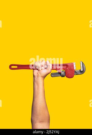 Worker's hand with red pipe wrench on yellow background. Labor day background concept Stock Photo