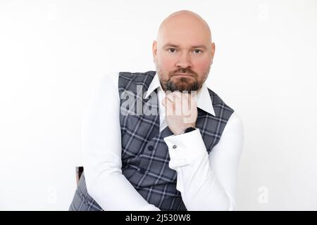 Portrait of serious middle-aged businessman in grey vest, white shirt sitting, putting chin on hand on white background. Stock Photo