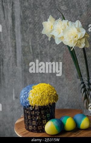Delicious Easter cake in the colors of the flag of Ukraine, yellow-blue colored Easter eggs on a wooden table with flowers in the background. place for text. selective focus. Stock Photo