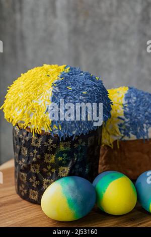 Delicious Easter cake in the colors of the flag of Ukraine, yellow-blue colored Easter eggs on a wooden table with flowers in the background. place for text. selective focus. Stock Photo