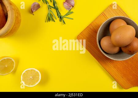 Garlic, eggs, and lemon spread out in composition to prepare the garlic-oil sauce typical of Spanish food on a yellow background. Stock Photo