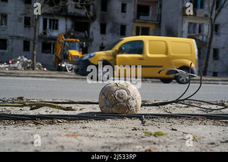 A children's soccer ball lies near the road against a building destroyed by an explosion in the war in Ukraine. Nearby are the wires of a broken power Stock Photo