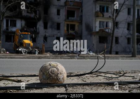 A children's soccer ball lies near the road against a building destroyed by an explosion in the war in Ukraine. Nearby are the wires of a broken power Stock Photo