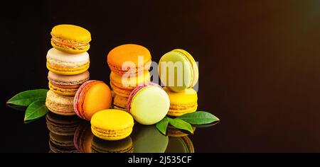 Sweet and colorful french macaroons.Banner of multicolored macaroons on a black background with fresh leaves.Kopy space. Stock Photo
