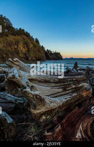 Sunset in Cape Disappointment state park.dramatic sun setting in rocky cliffs and light house with massive drift wood logs on the bay Area. Stock Photo