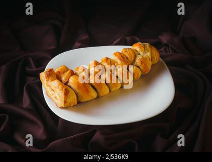 Homemade braided bread filled with strawberry jam on a white plate with rustic black background, gourmet bakery. Traditional Mexican sweet bread. Stock Photo