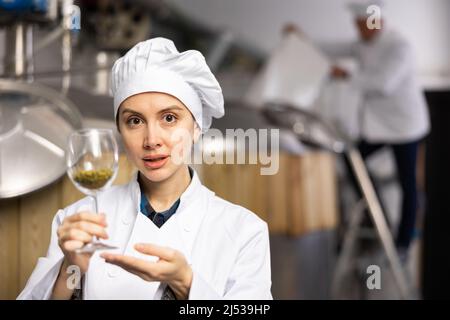 Successful female brewmaster showing hop pellets in glass Stock Photo