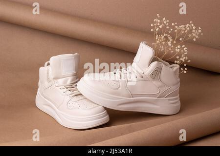 Eco leather shoes. A pair of beige sneakers with dry flowers on brown background. Casual sport lifestyle concept. Stock Photo