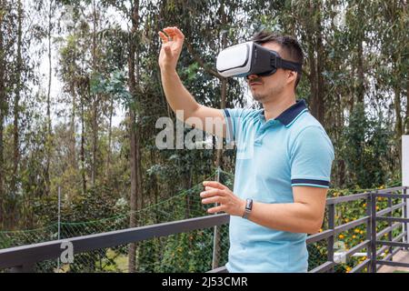 Caucasian young man using virtual reality glasses on a terrace in the middle of trees outdoors Stock Photo