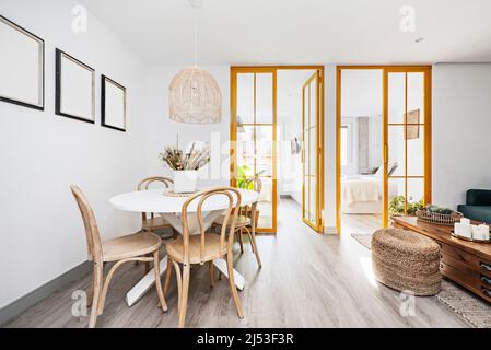 Modern decorated living room with circular white wooden dining table, wicker seat, wooden chairs and stained glass windows with yellow metal Stock Photo