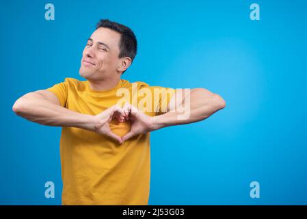 Smiling man gesturing heart on chest in blue studio Stock Photo