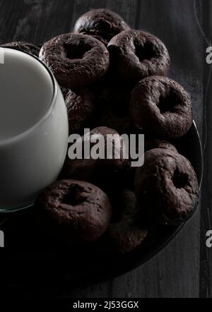 A black plate with small baby chocolate donuts lit by the morning sunlight, with an ice milk on the side and on a wooden table. Stock Photo