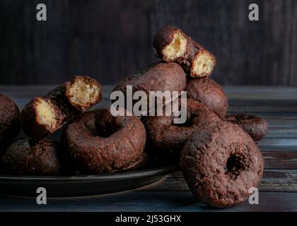 A black plate with small baby chocolate donuts on a wooden table and a rustic wooden background Stock Photo