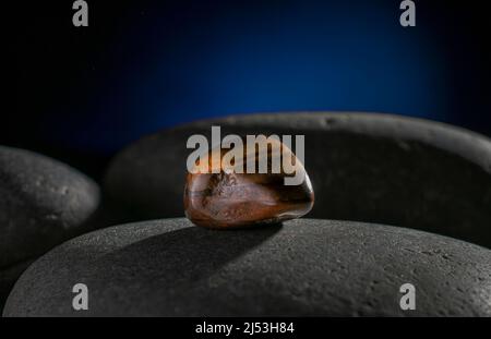 Eye of a tiger stone, on a rock in the darkness  with a rim light and a dark blue background Stock Photo