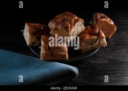 dark food photography, cinnamon rolls with raisins on a black plate with a blue napkin over a rustic table. Chiaroscuro food photography Stock Photo