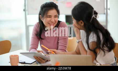 Two attractive asian female enjoy chatting, laughing, having fun during working together on the project in the office. Stock Photo