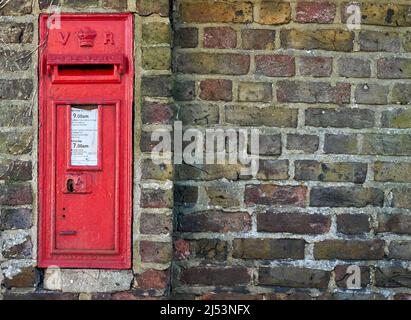 A red British post box in a wall with the royal cypher VR Stock Photo