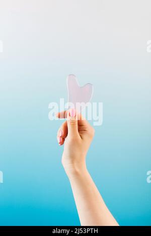 A woman holds a gouache jade massage scraper in her hand. Trendy beauty treatments. Copy space. Stock Photo