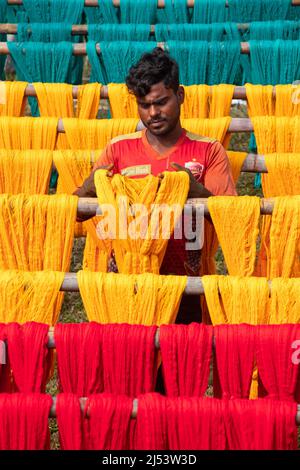Narayanganj, Dhaka, Bangladesh. 20th Apr, 2022. A worker hangs thousands of freshly dyed colorful threads on a wooden structure as they are being dried in the sunshine in Narayanganj, Bangladesh. Thousands of colorful threads create a palette of colors as workers hang them out to dry. The threads take a whole day to dry and stretch for hundreds of meters. Once dried, they are sold to wholesale markets. Each row of threads is priced for Â£2. The workers spend 12 hours in the fields during this process, earning Â£5 per day. (Credit Image: © Joy Saha/ZUMA Press Wire) Stock Photo