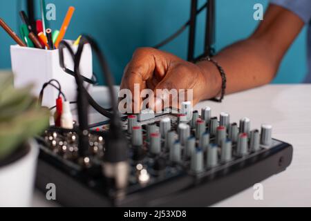 Closeup of content creator hand adjusting master volume fader on mixer console on desk during live podcast. Vlogger working on sound settings of equilizer used to broadcast live stream. Stock Photo
