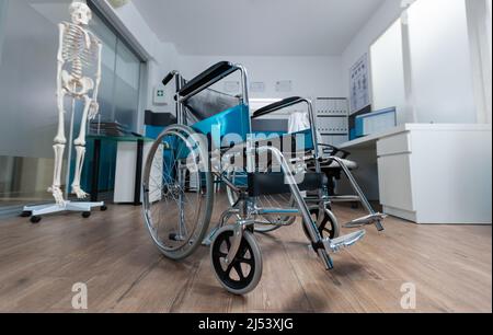Medical wheelchair standing in empty doctor office used for invalid patient during illness examination. Hospital room equipped with professional instruments. Health care services support Stock Photo
