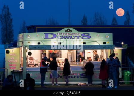 Pink moon rising over a fresh donuts vendor at an outside 1980s retro festival concert in Southend on Sea, Essex, UK. Food stall Stock Photo