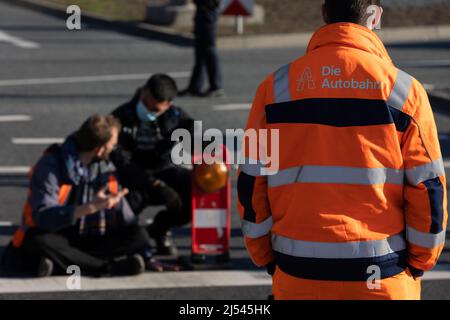 Offenbach, Germany. 20th Apr, 2022. An activist has stuck his hand on the roadway in protest, which is why the police have to regulate traffic around the activist. Activists of the 'Last Generation' blocked the highway exit in Offenbach-Kaiserlei. Credit: Hannes P. Albert/dpa/Alamy Live News Stock Photo