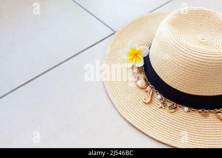 Summer beach straw hat with a necklace with shells and pearls and the plumeria flower on the tiled floor with copy space. The concept of summer vacati Stock Photo