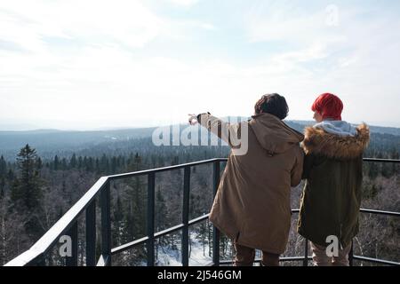 Young man and woman in love standing at observation deck somewhere in mountains looking at landscape on winter day Stock Photo